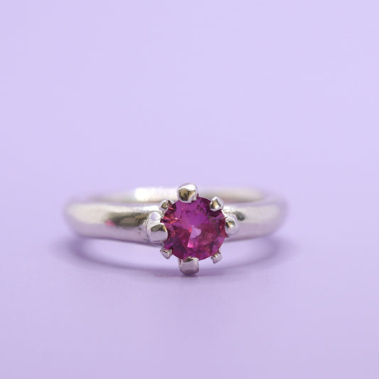 Silver ring with a pink gemstone on a light purple background