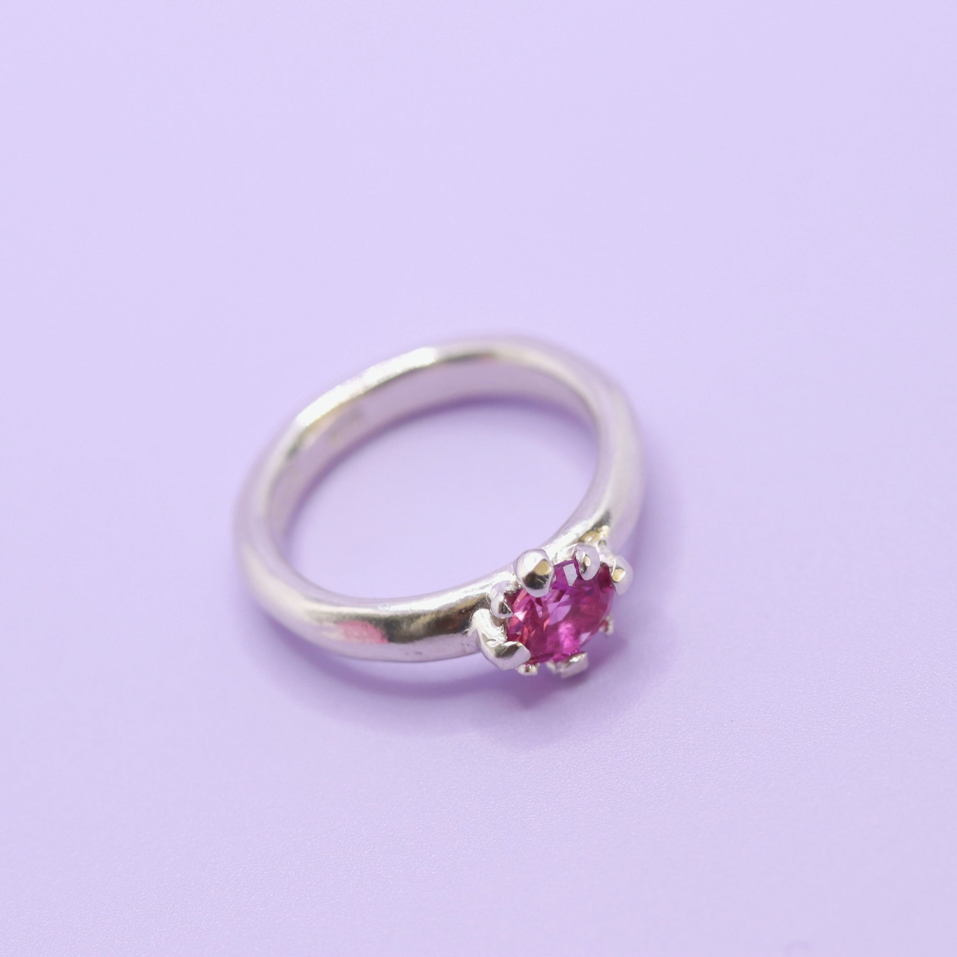 Silver ring with a pink gemstone on a light purple background