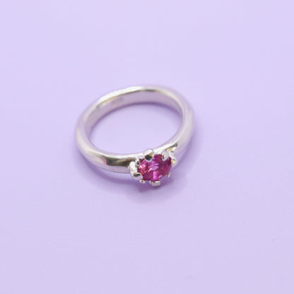 Silver ring with a pink gemstone on a light purple background