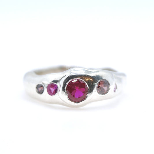 Silver ring with red and pink gemstones on a white background