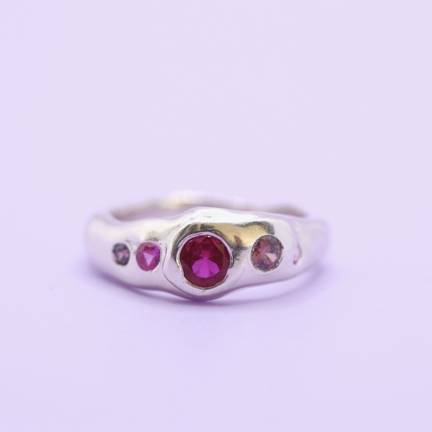 Silver ring with red and pink gemstones on a light purple background