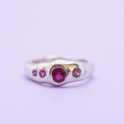 Silver ring with red and pink gemstones on a light purple background
