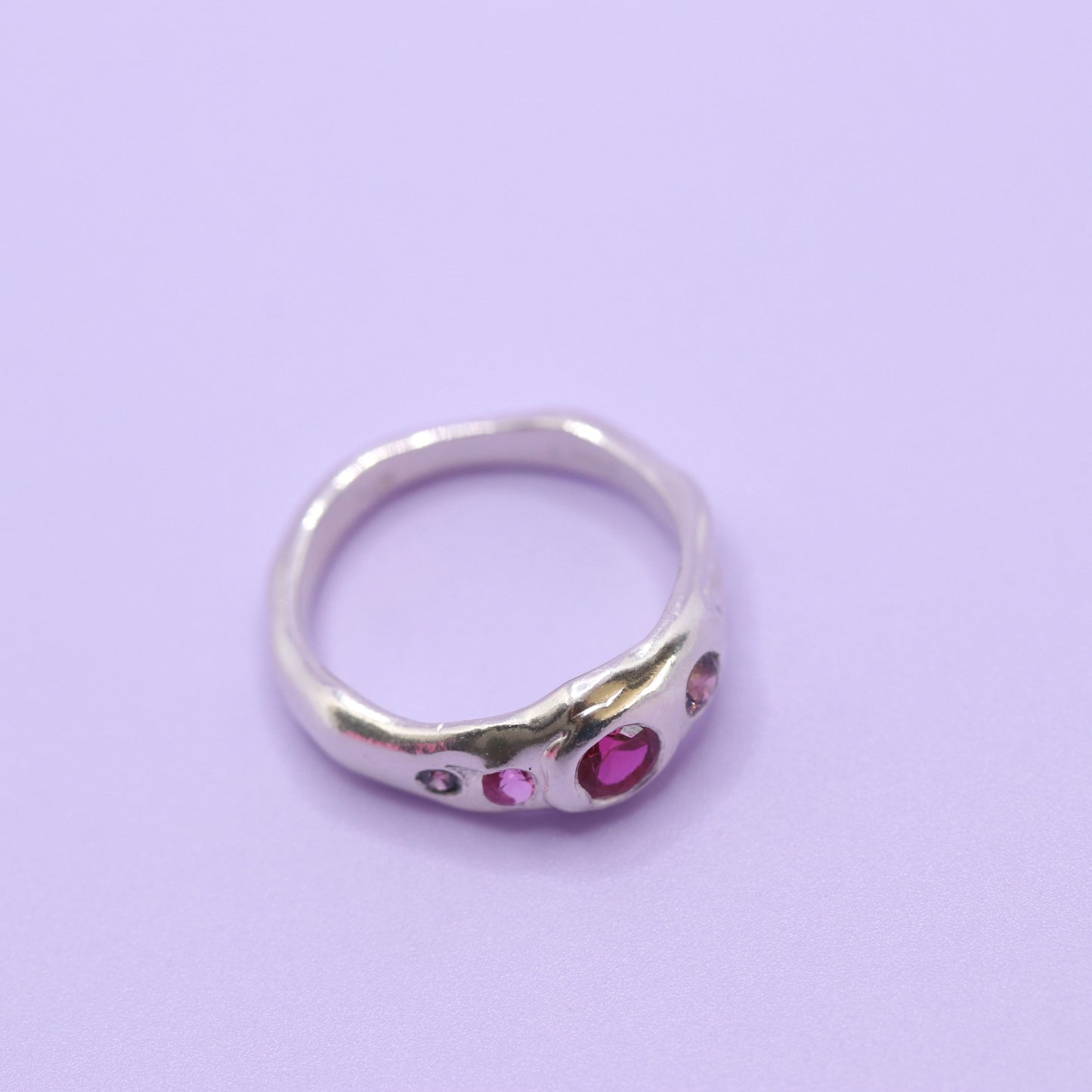 Silver ring with pink gemstones on a light purple background