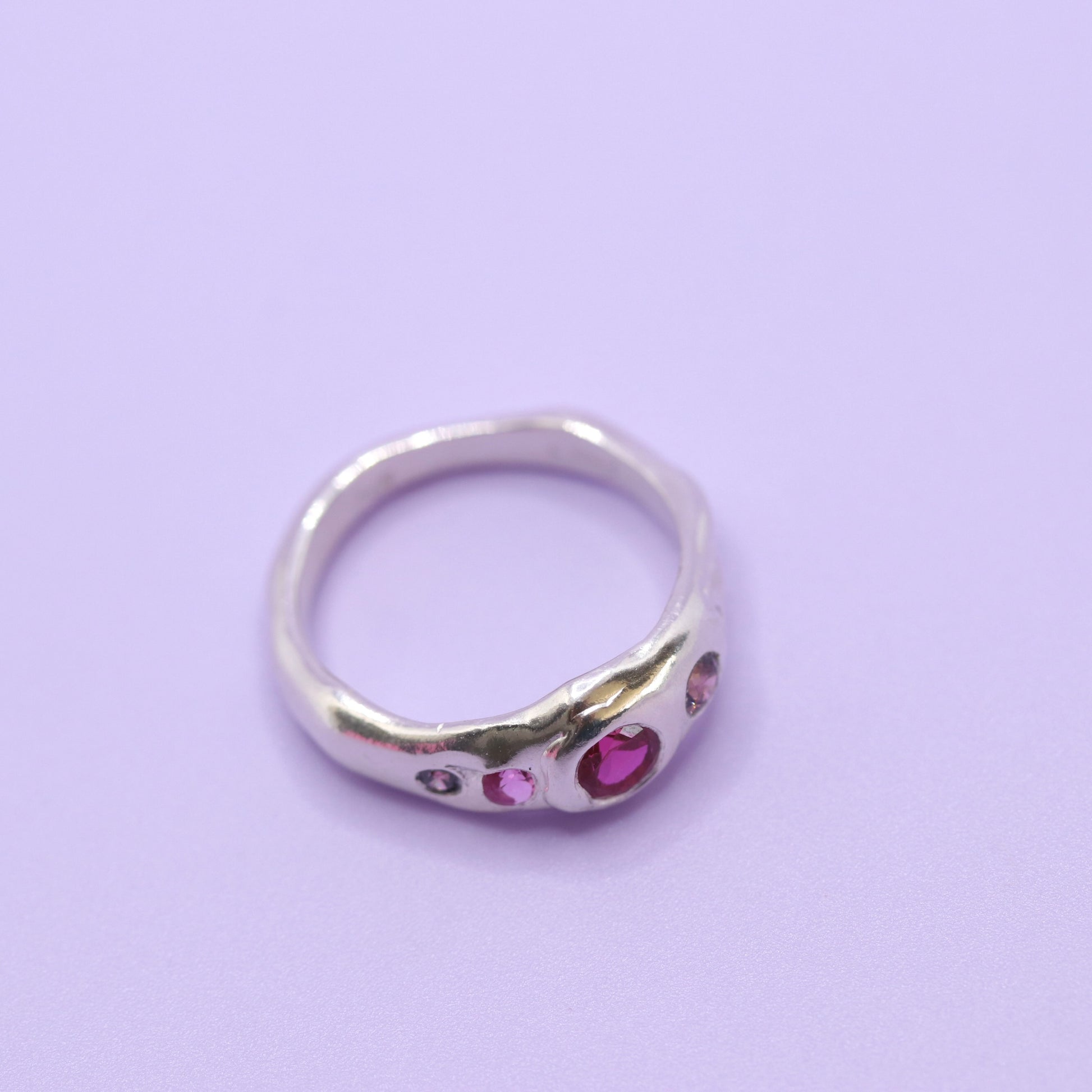 Silver ring with pink gemstones on a light purple background