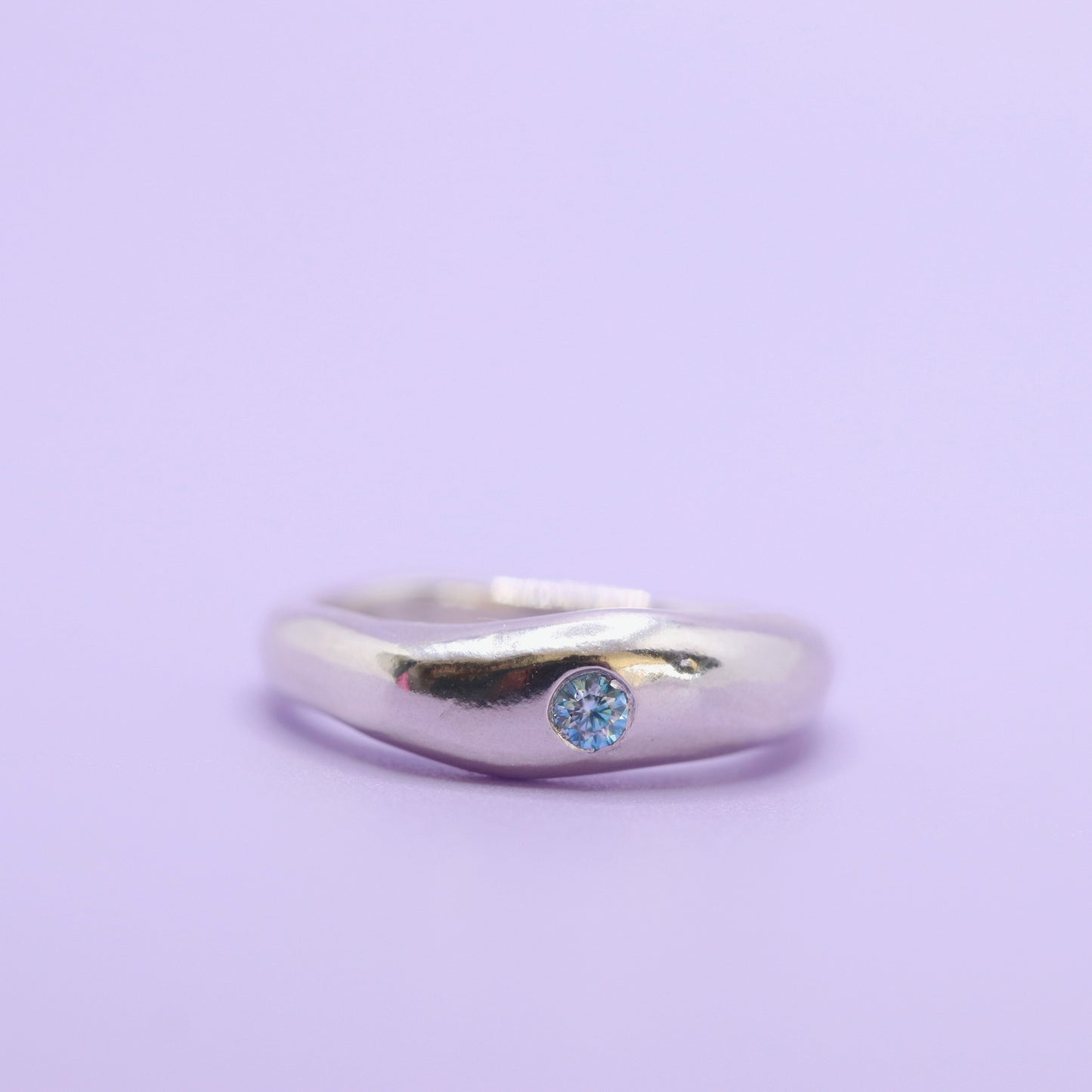 Silver ring with a blue gemstone on a light purple background