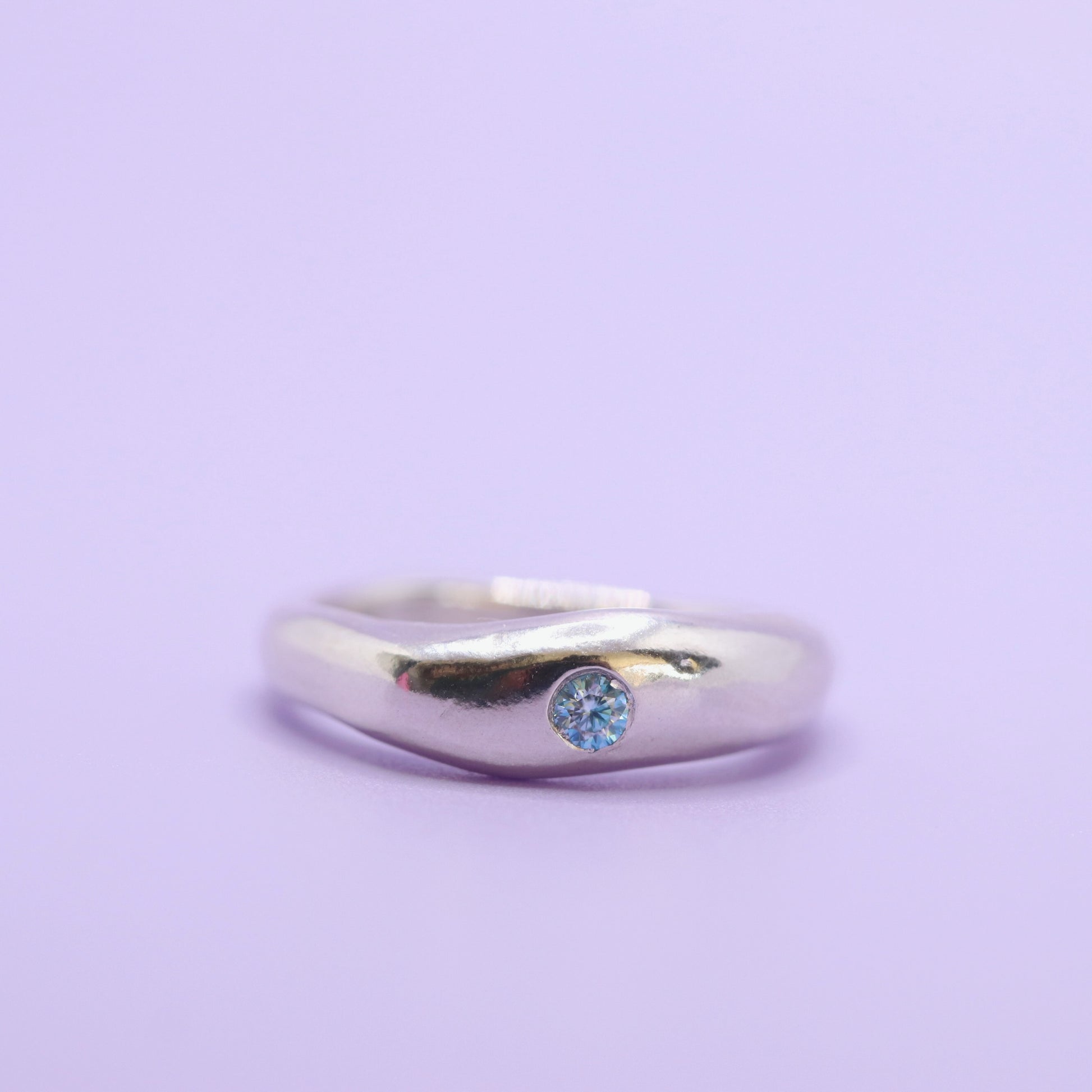 Silver ring with a blue gemstone on a light purple background
