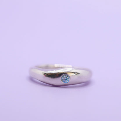 Silver ring with a blue gemstone on a light purple background