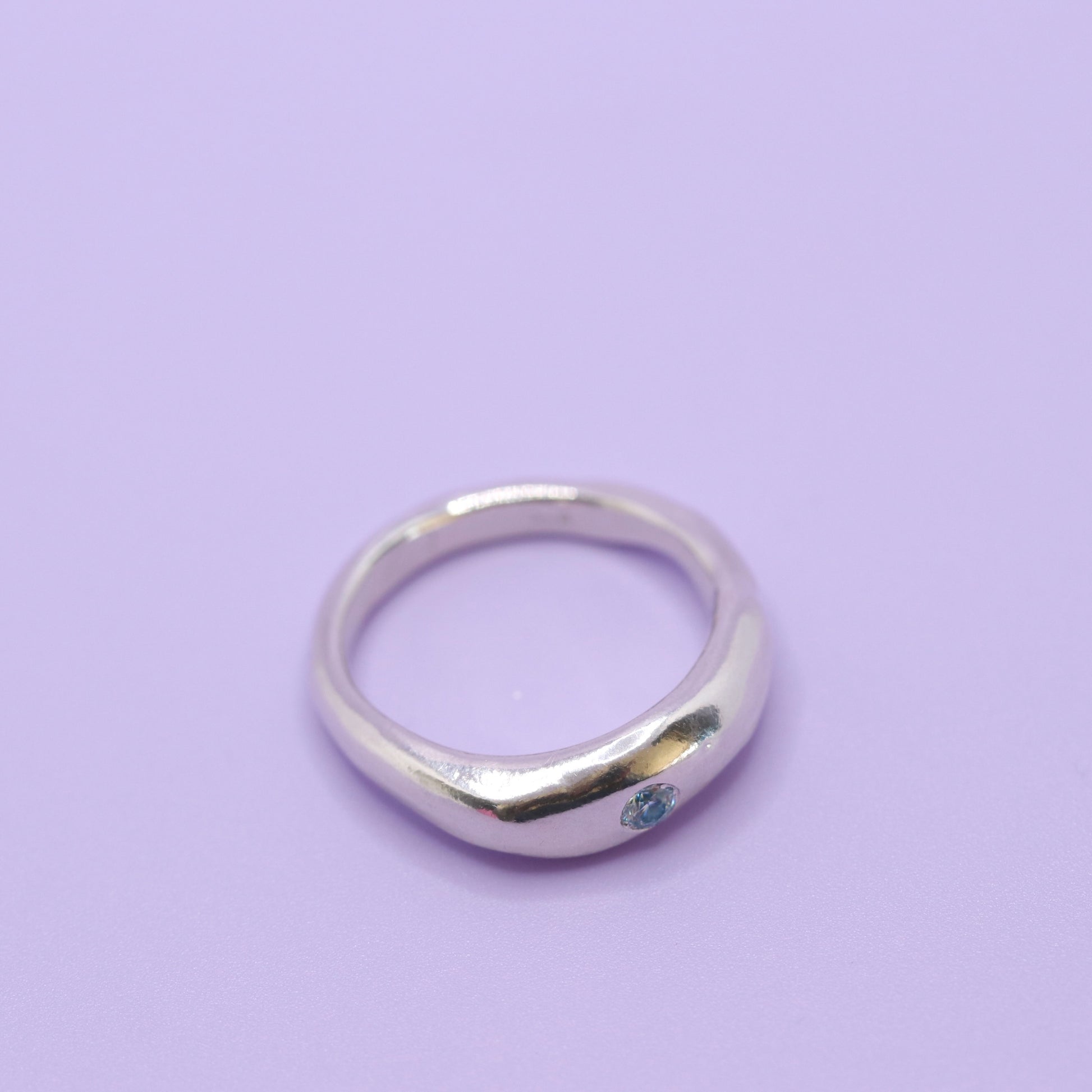 Silver ring with a blue gemstone on a light purple background