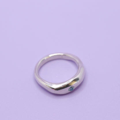 Silver ring with a blue gemstone on a light purple background