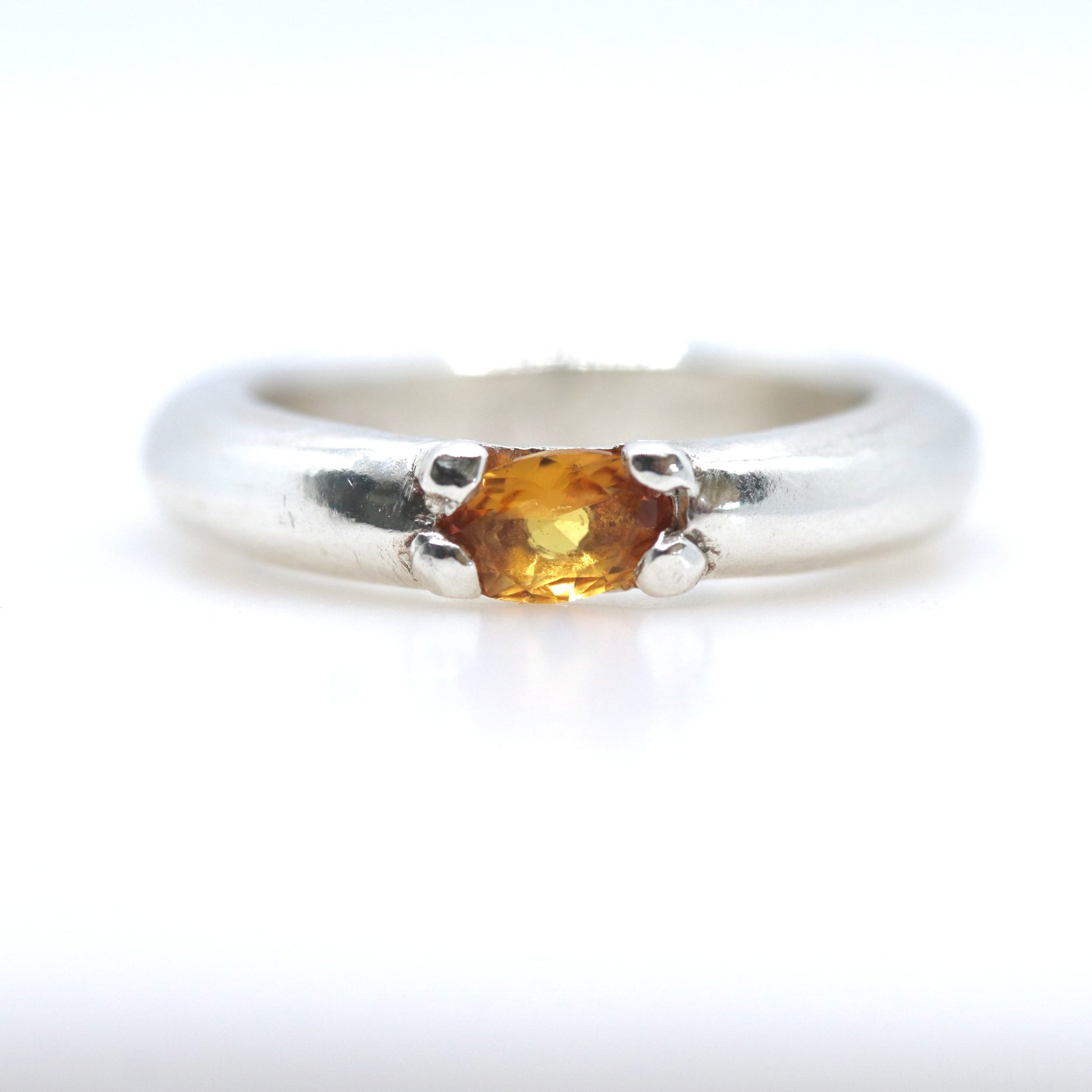 A silver ring featuring a small, oval-cut amber gemstone in a prong setting, shown against a plain white background.