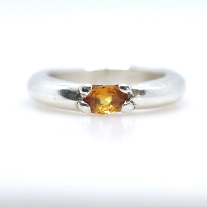 A silver ring featuring a small, oval-cut amber gemstone in a prong setting, shown against a plain white background.