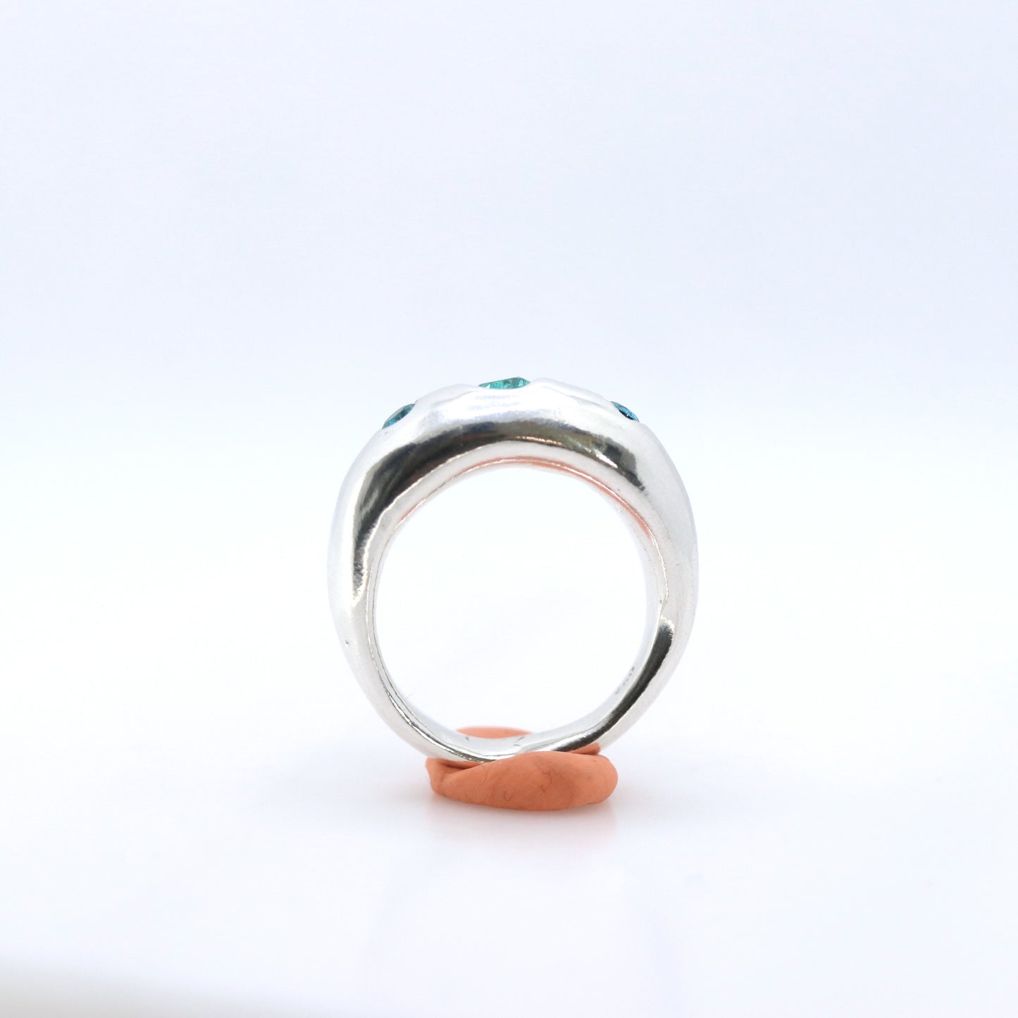 A polished silver ring with small green gemstone accents on the shoulders, displayed on orange tack against a white background.