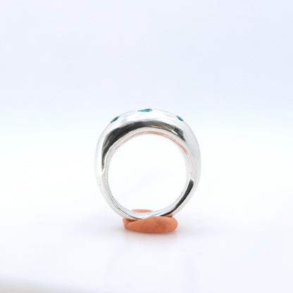 A polished silver ring with small green gemstone accents on the shoulders, displayed on orange tack against a white background.