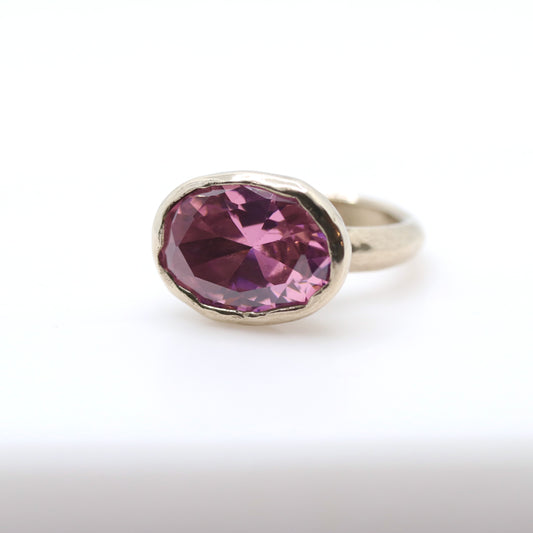 A silver ring featuring an irregular, faceted oval gemstone in a dusty pink hue, set against a clean white background.