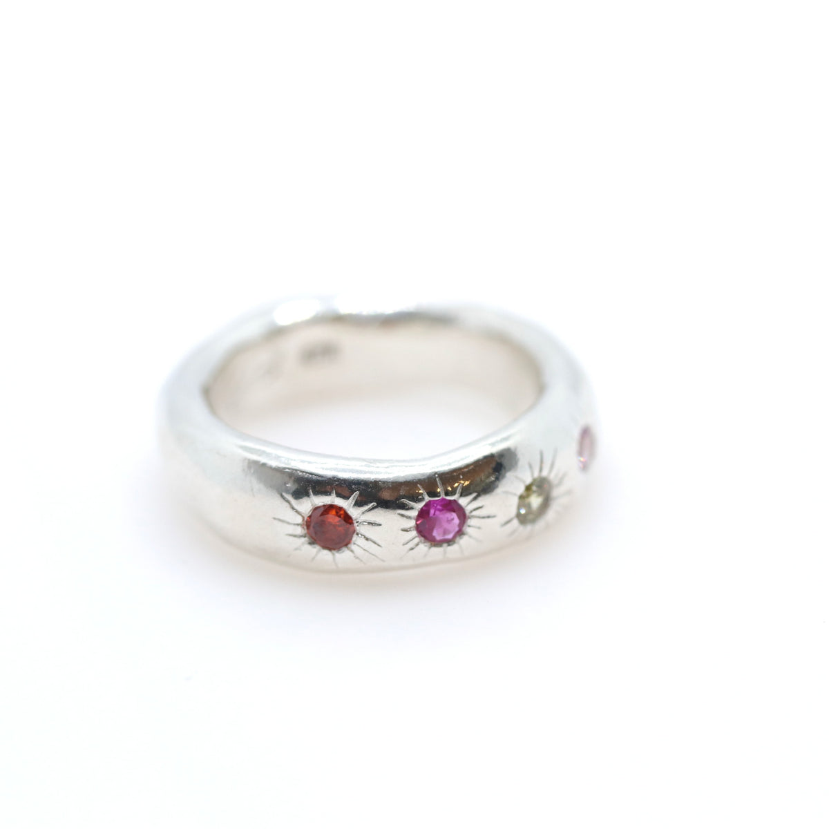 A sterling silver band ring featuring three small sunburst motifs set with colorful gemstones in red, pink, and green, shown on a plain white background.