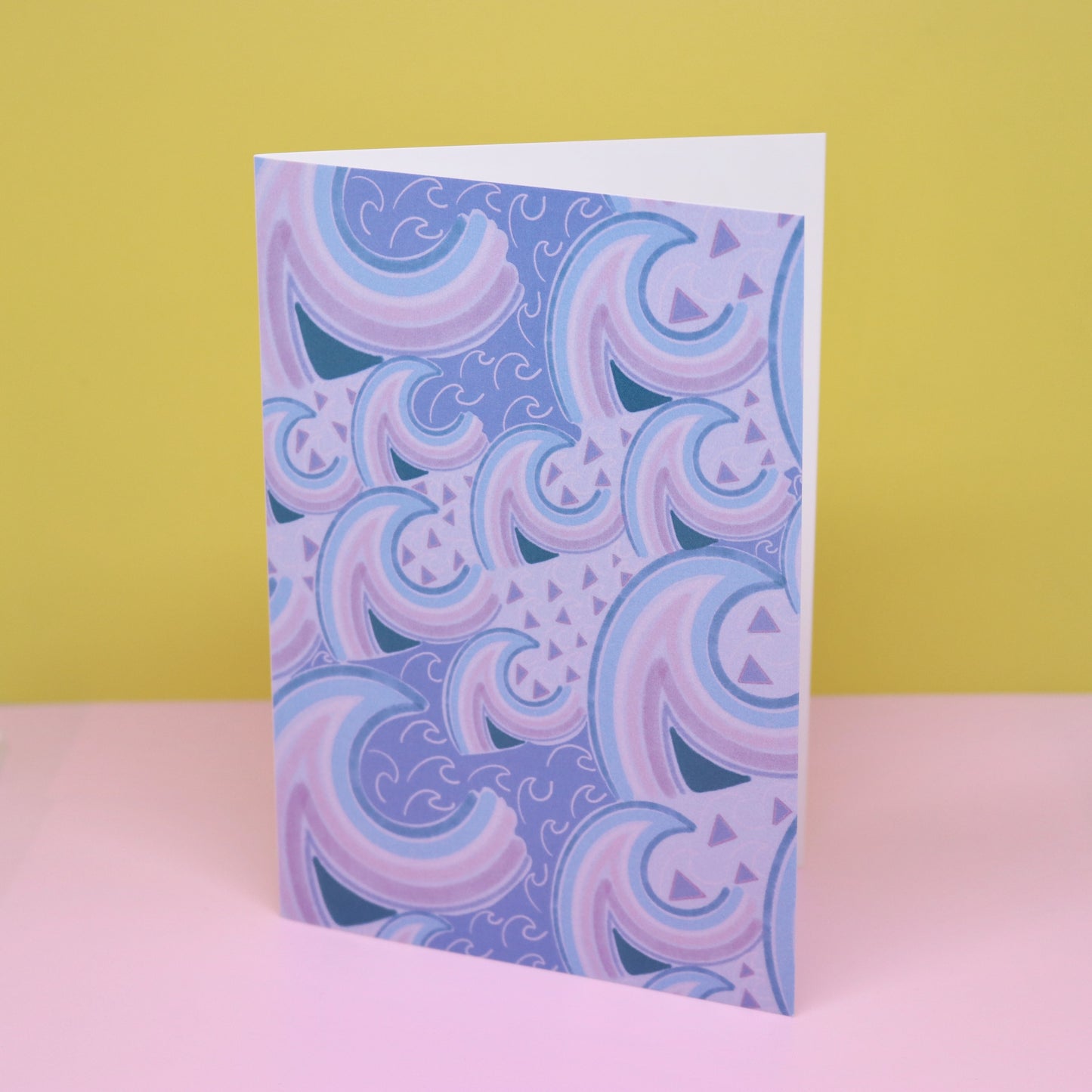 Card with purple and blue wave pattern on a pink surface and yellow background. New Zealand made illustrated greeting card with wave print