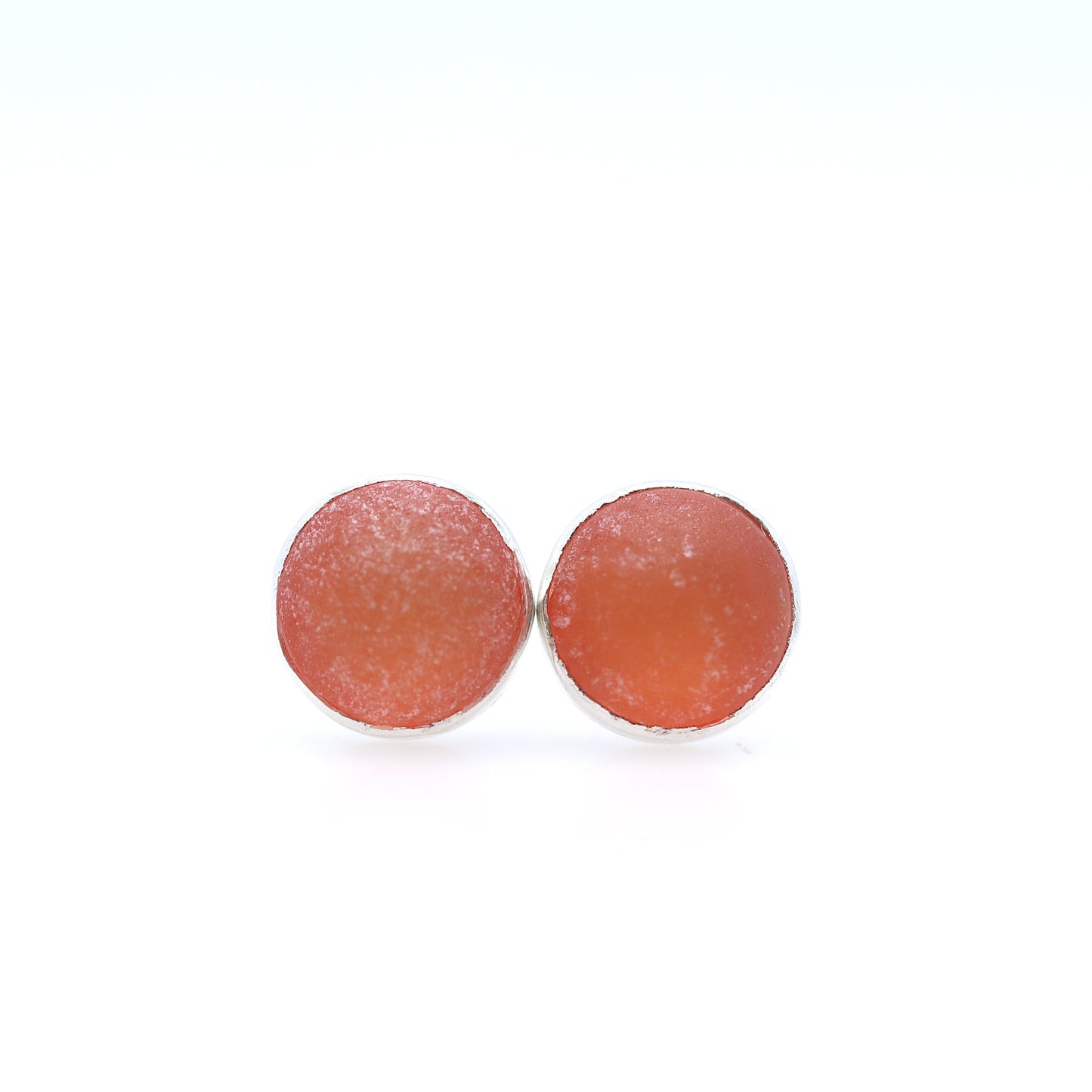 Round earrings with a textured tangerine dome on a white background