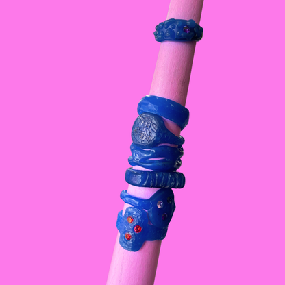 A set of textured blue wax rings displayed on a light pink cylindrical stand against a solid pink background.