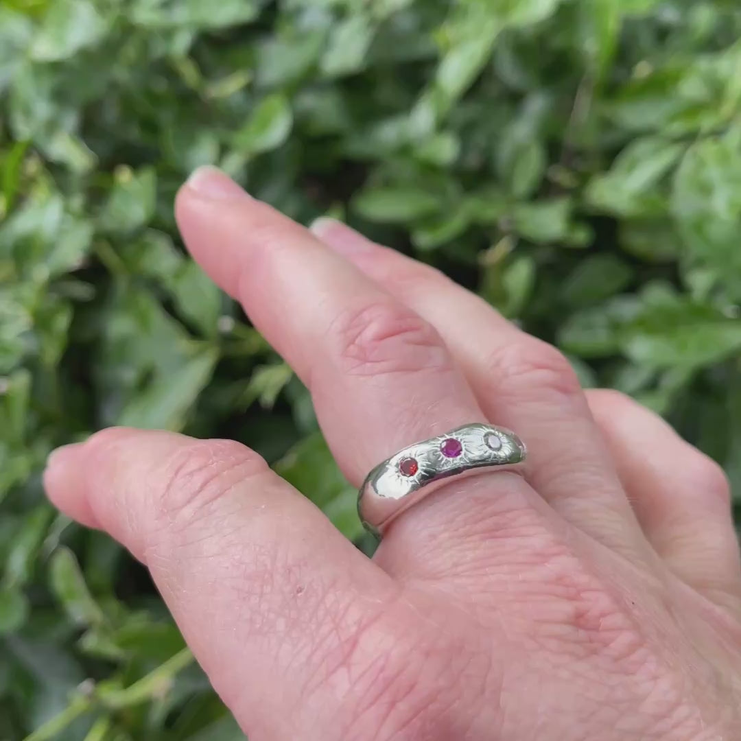 Silver ring with four colourful gems on hand with leafy background